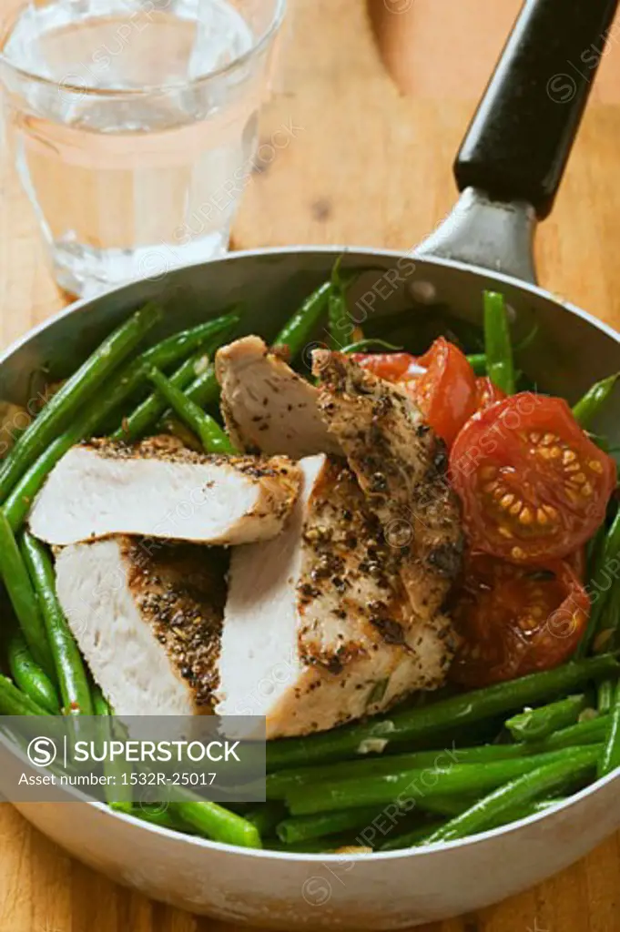 Chicken breast with green beans and tomatoes in frying pan