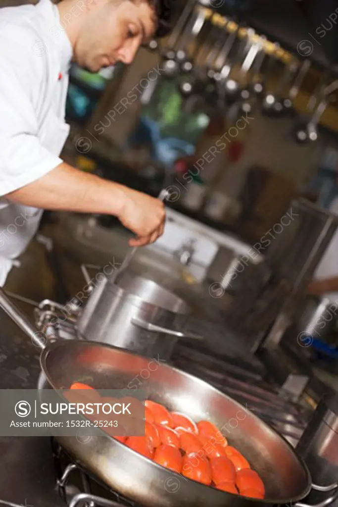 Tomatoes in frying pan, chef stirring pan