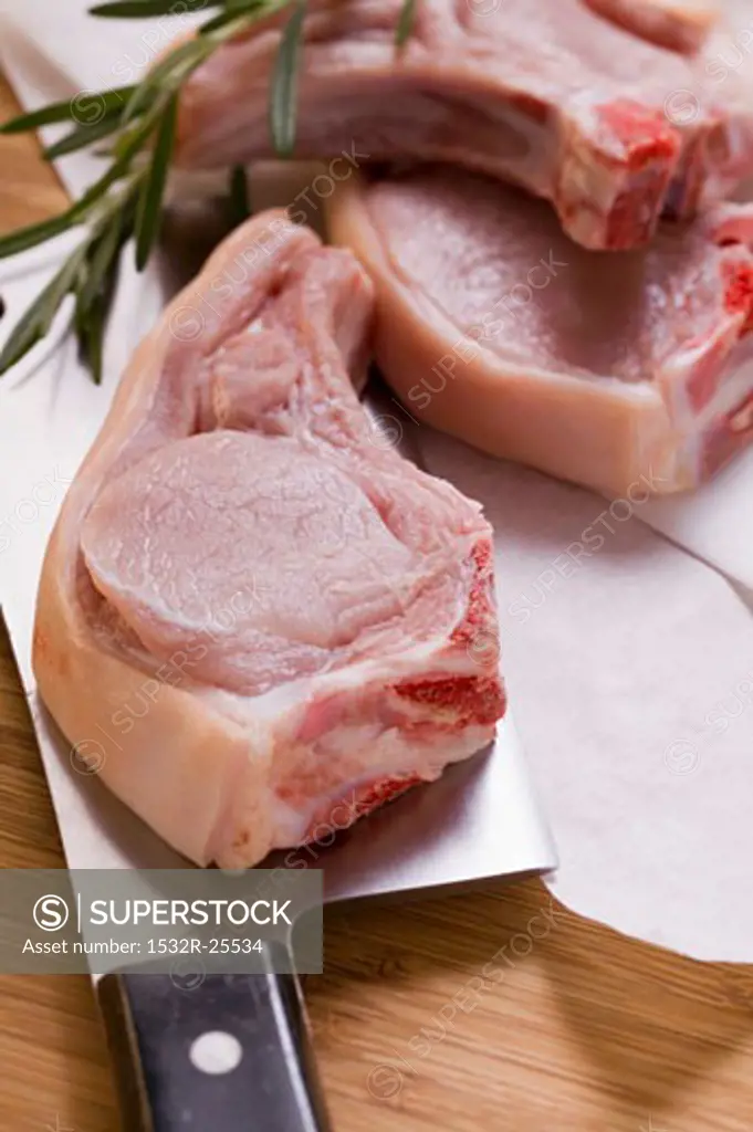 Raw pork chops with meat cleaver and rosemary