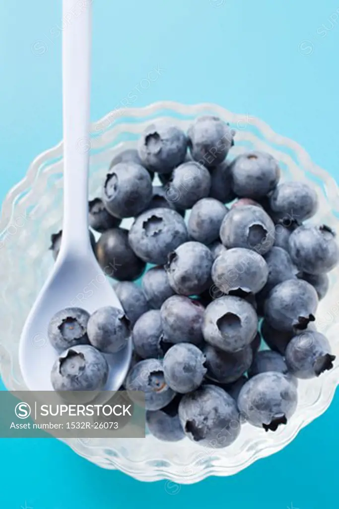Fresh blueberries in glass bowl with spoon (overhead view)