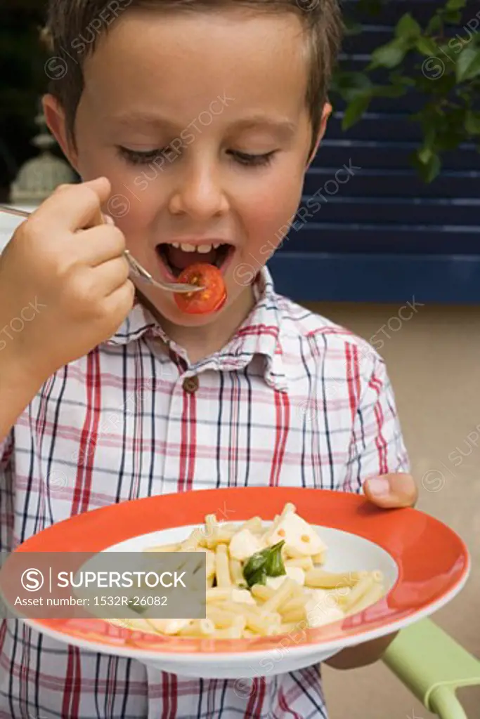 Small boy eating pasta with tomatoes