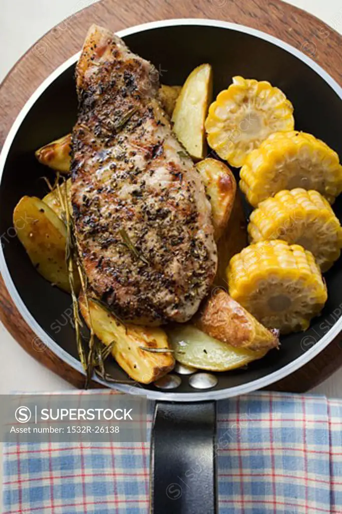 Pork chop with fried potatoes and sweetcorn in frying pan