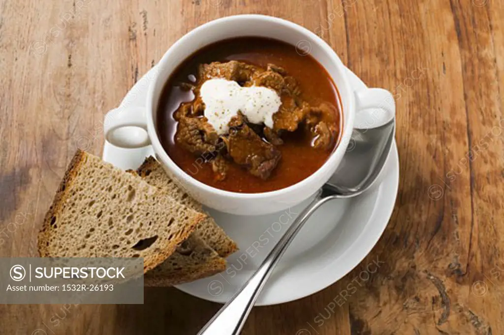 Goulash soup with sour cream in soup cup, slices of bread