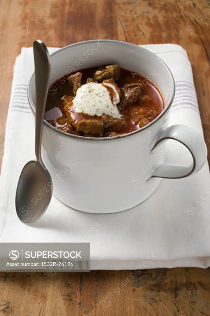 Goulash soup with sour cream in cup, with spoon