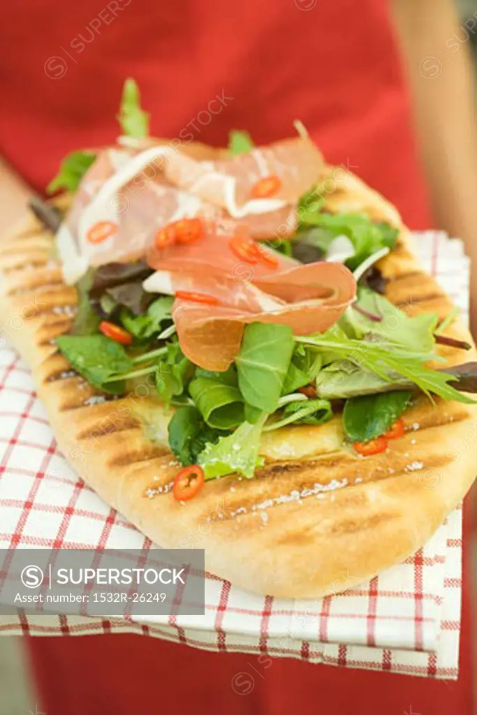 Woman holding pizza bread topped with Parma ham, herbs, chilli rings