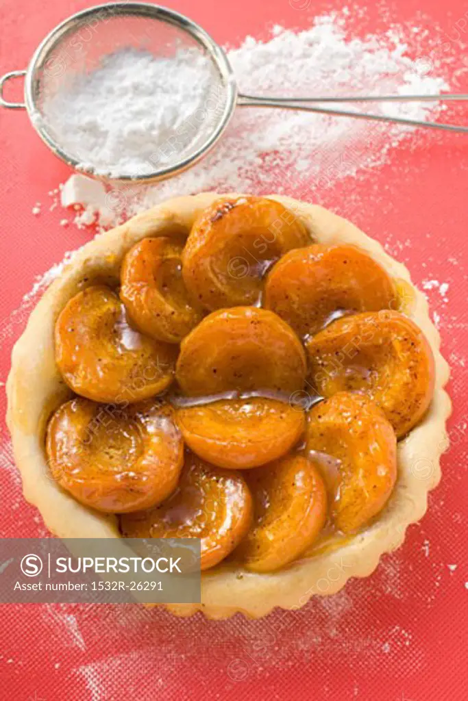 Apricot tart, icing sugar in sieve beside it