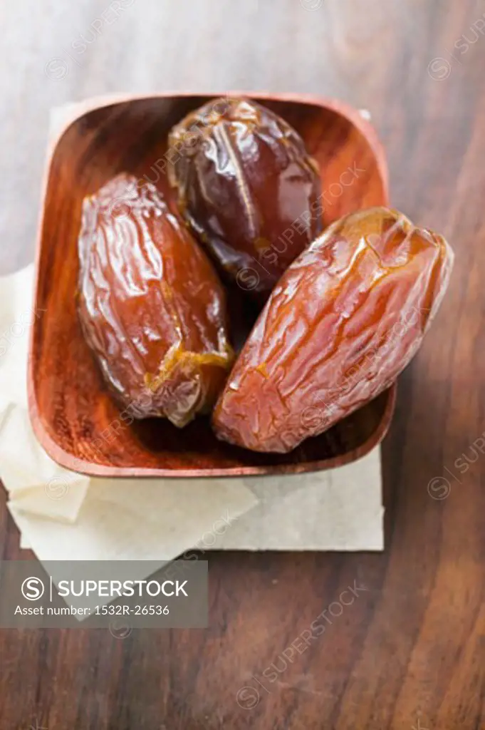Three dried dates in wooden bowl