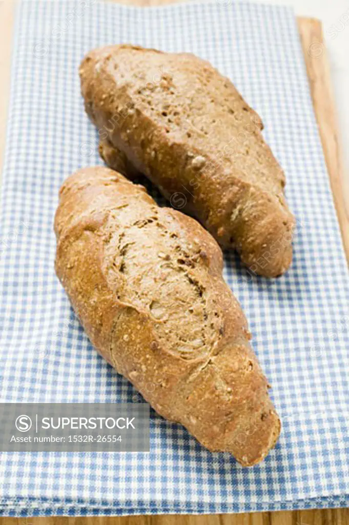 Two Kornspitz bread rolls on blue and white checked cloth