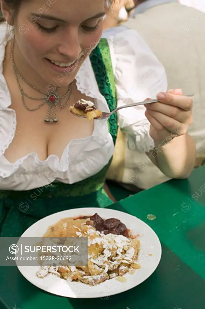 Woman eating scrambled pancake with plum compote at Oktoberfest