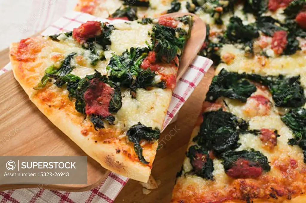 Spinach, tomato and cheese pizza with slice on server
