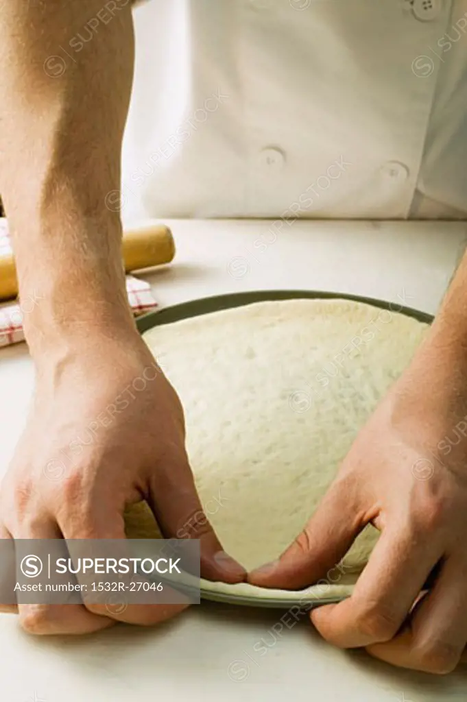 Pressing pizza dough into baking tin