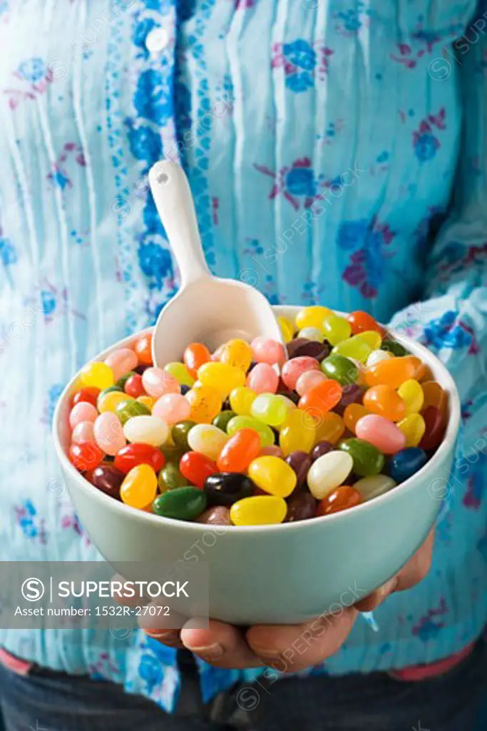 Hand holding bowl of coloured jelly beans with scoop