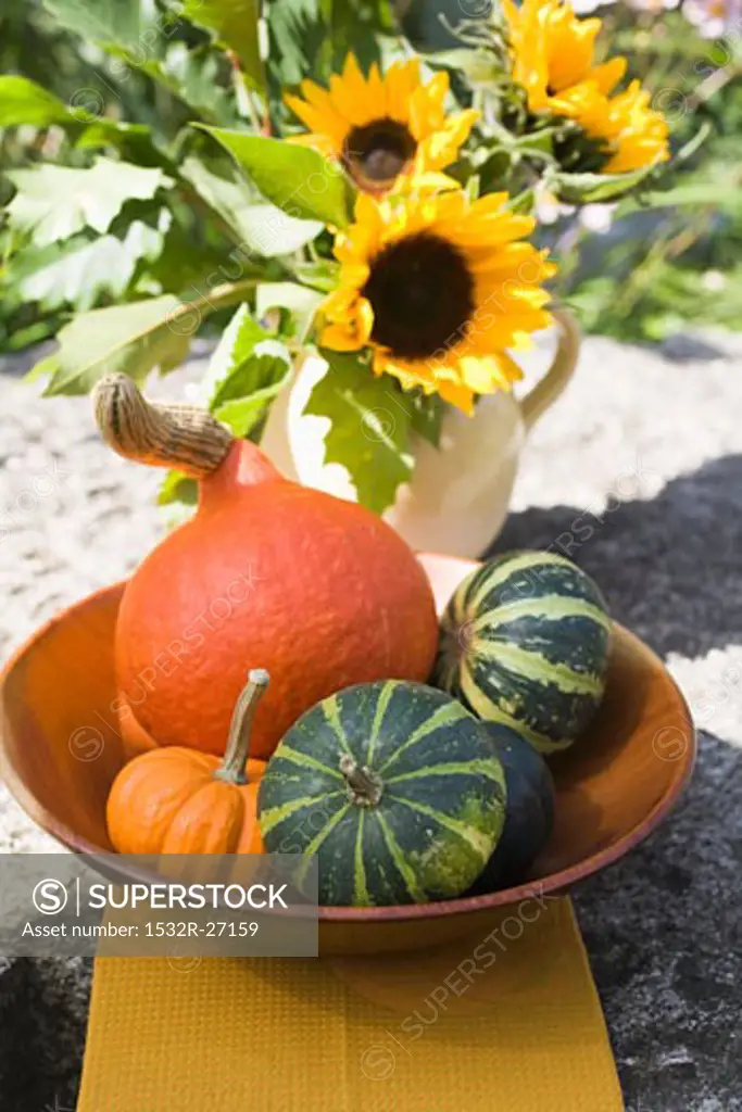 Assorted squashes in bowl and sunflowers in the open air