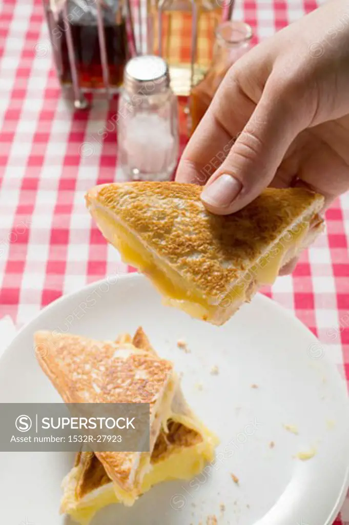 Hand holding a piece of toasted cheese sandwich