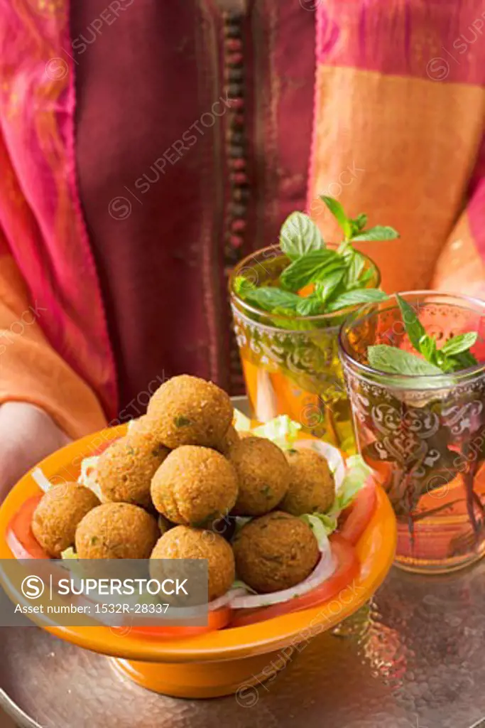 Woman holding tray of falafel (chick-pea balls) and tea
