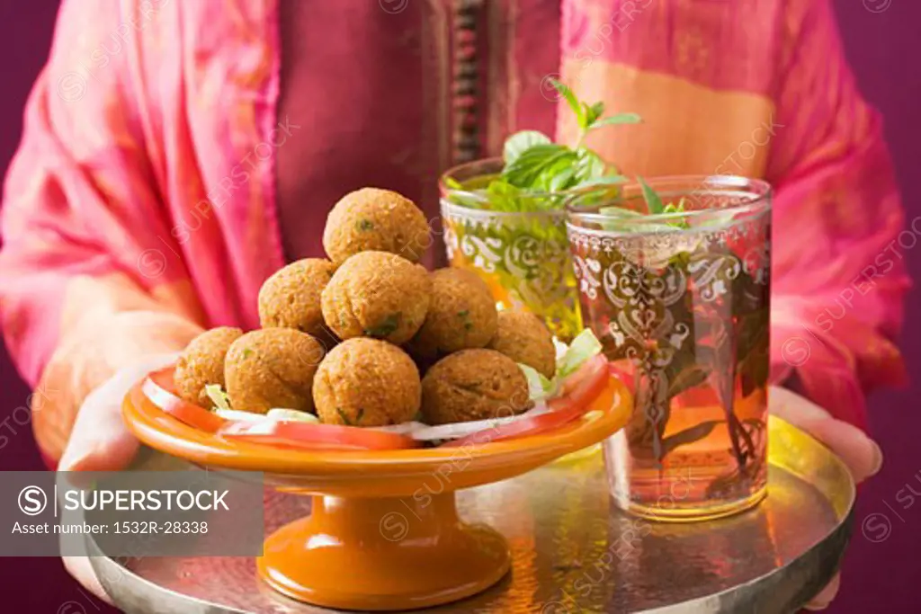 Woman holding tray of falafel (chick-pea balls) and tea