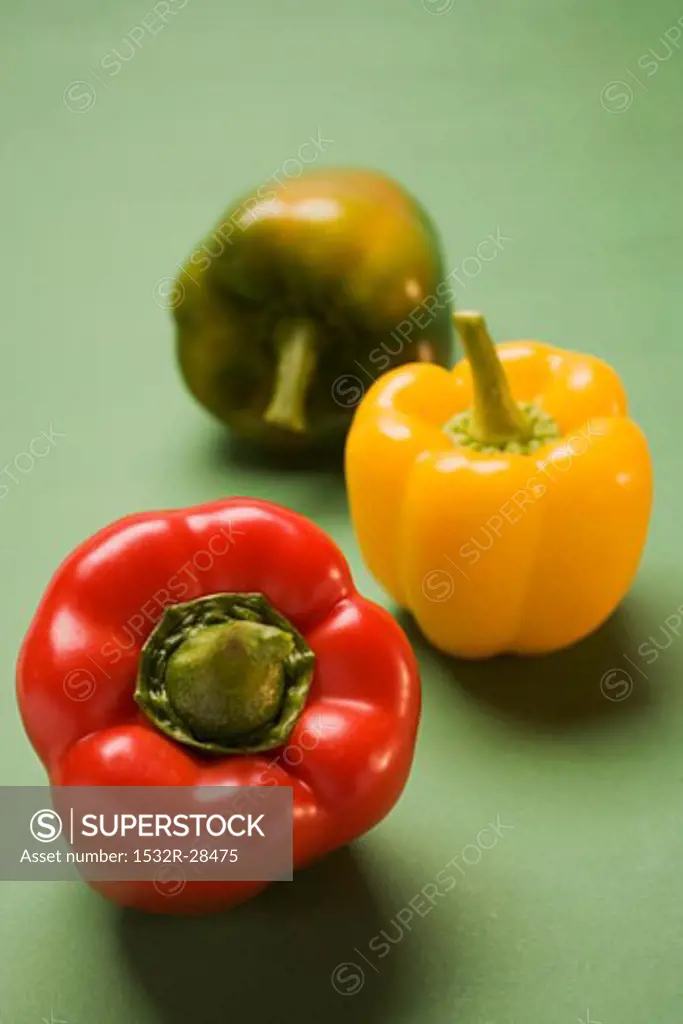 Three peppers (yellow, red, green) on green background