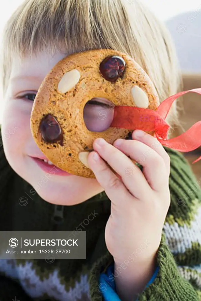 Small boy holding gingerbread tree ornament in front of his face