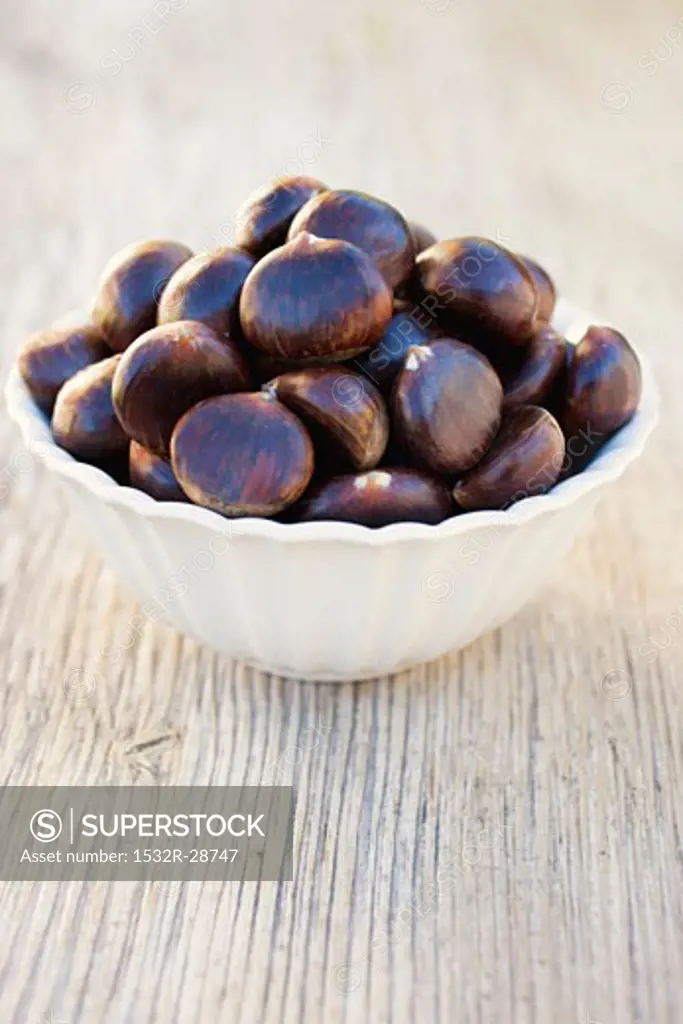 Chestnuts in white bowl on wooden background