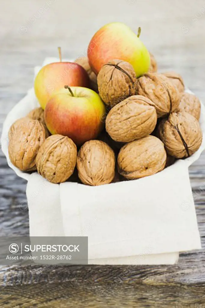 Walnuts and apples on cloth in white bowl