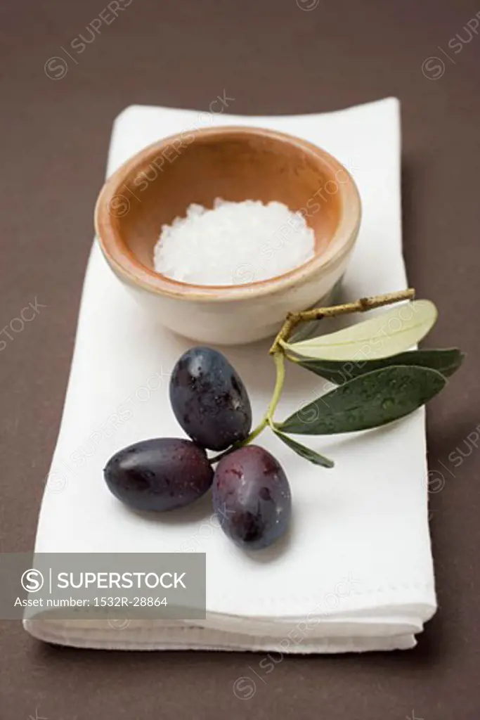 Black olives on twig, sea salt in terracotta bowl