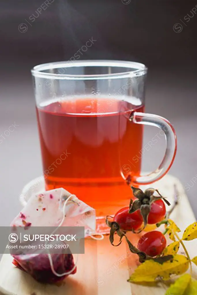 Rose hip tea in glass cup, fresh rose hips and tea bag