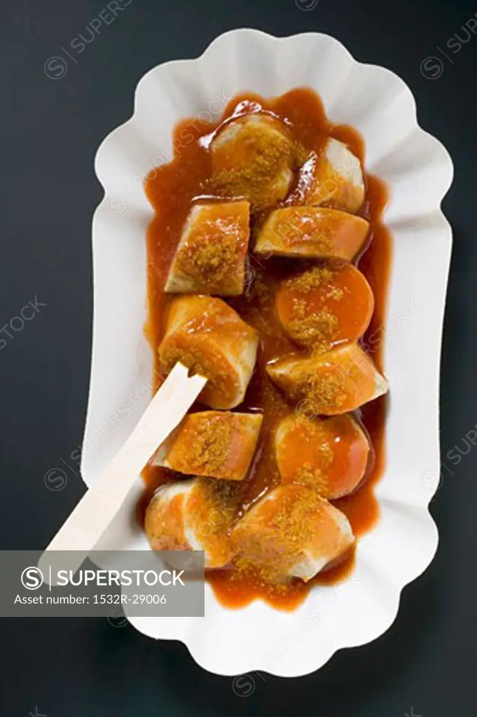 Sausage with ketchup & curry powder in paper dish (overhead)