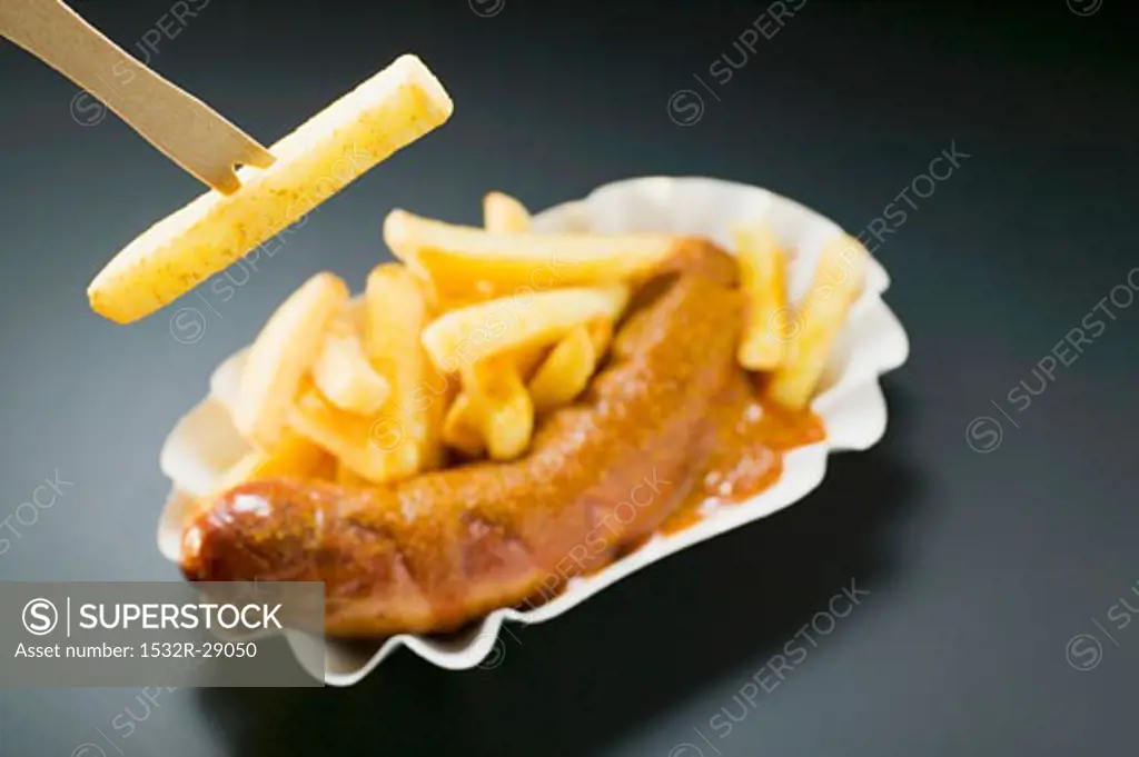 Ssausage with ketchup & curry powder & chips, one on wooden fork