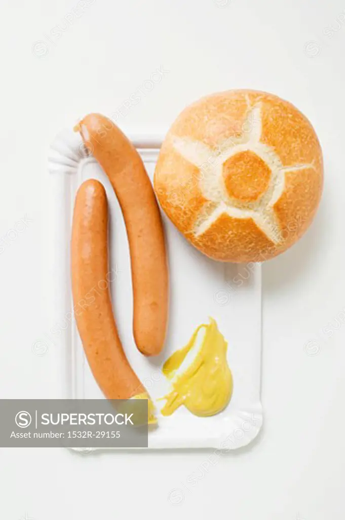 Frankfurters, bread roll and mustard on paper plate