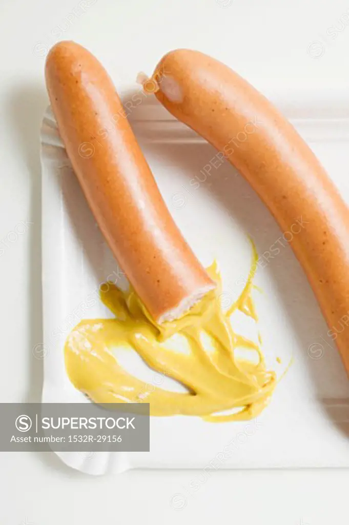 Frankfurters, partly eaten, with mustard on paper plate