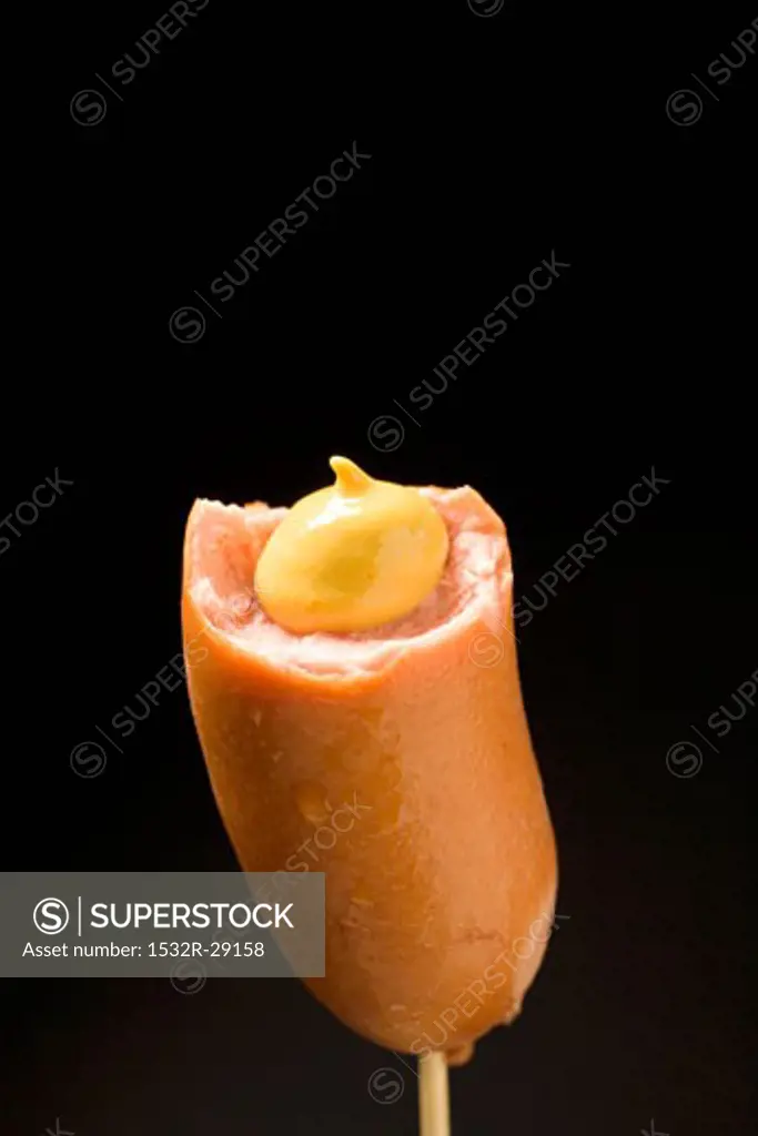 Frankfurter, partly eaten, with mustard on cocktail stick
