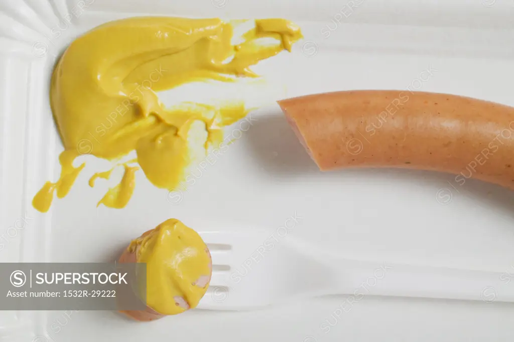 Frankfurter with mustard on paper plate