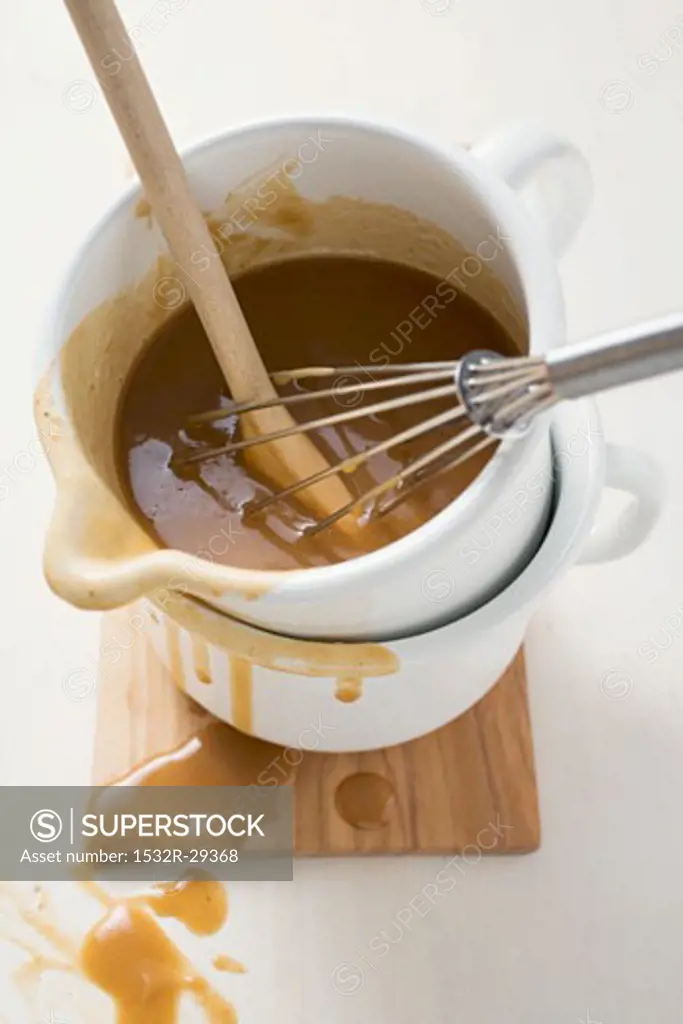 Gravy in an enamel jug with wooden spoon and whisk