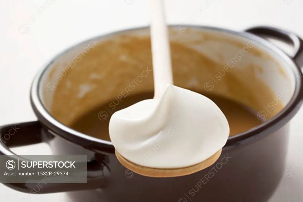 Gravy in pan, wooden spoonful of crème fraîche resting on pan