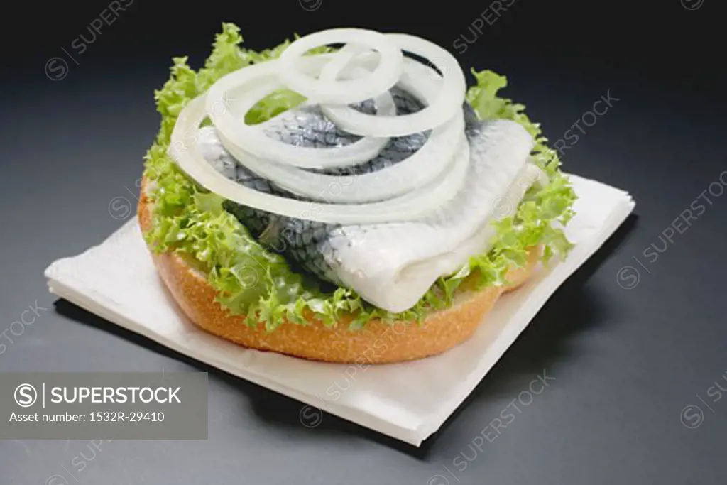 Half bread roll topped with herring & onions on paper napkin
