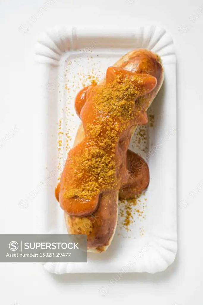 Sausage with ketchup and curry powder on paper plate