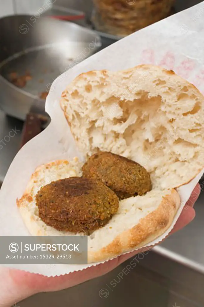 Hand holding pita bread filled with falafel (chick-pea balls)