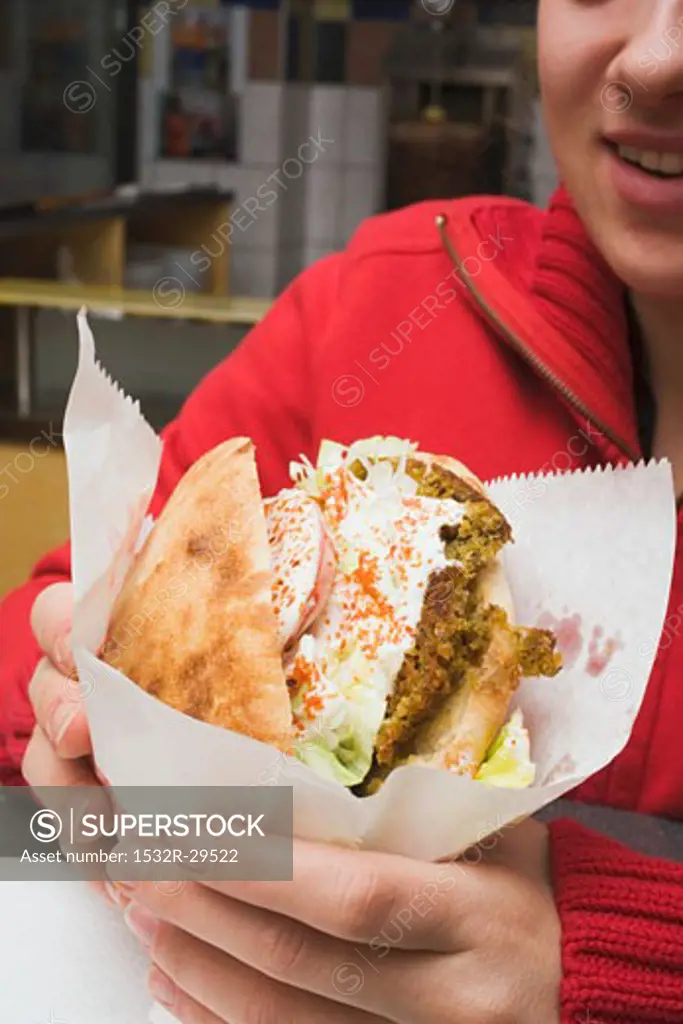 Person holding pita bread filled with falafel in snack bar