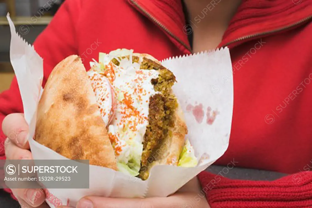 Person holding pita bread filled with falafel in snack bar