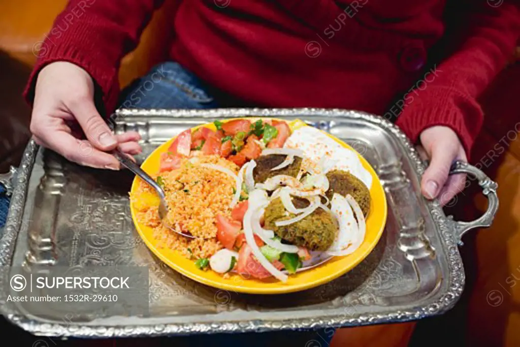 Person holding falafel with accompaniments on tray (N. Africa)
