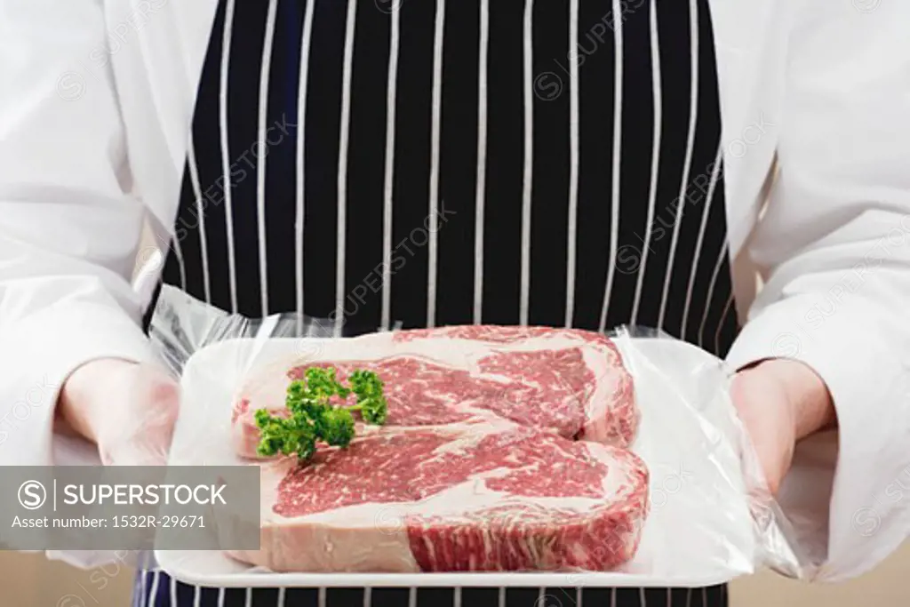 Person holding two sirloin steaks on tray