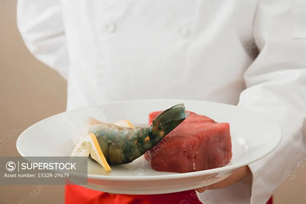Chef holding beef fillet, king prawn and lemon on plate