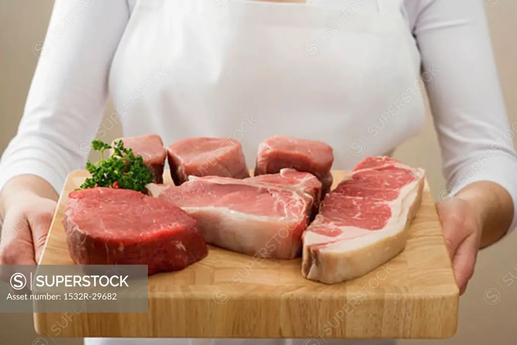 Person holding beef steaks & pork fillet on chopping board