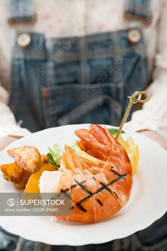 Person holding grilled king prawn on plate