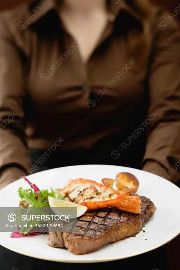 Woman holding plate of Surf & Turf (beef steak with prawn)
