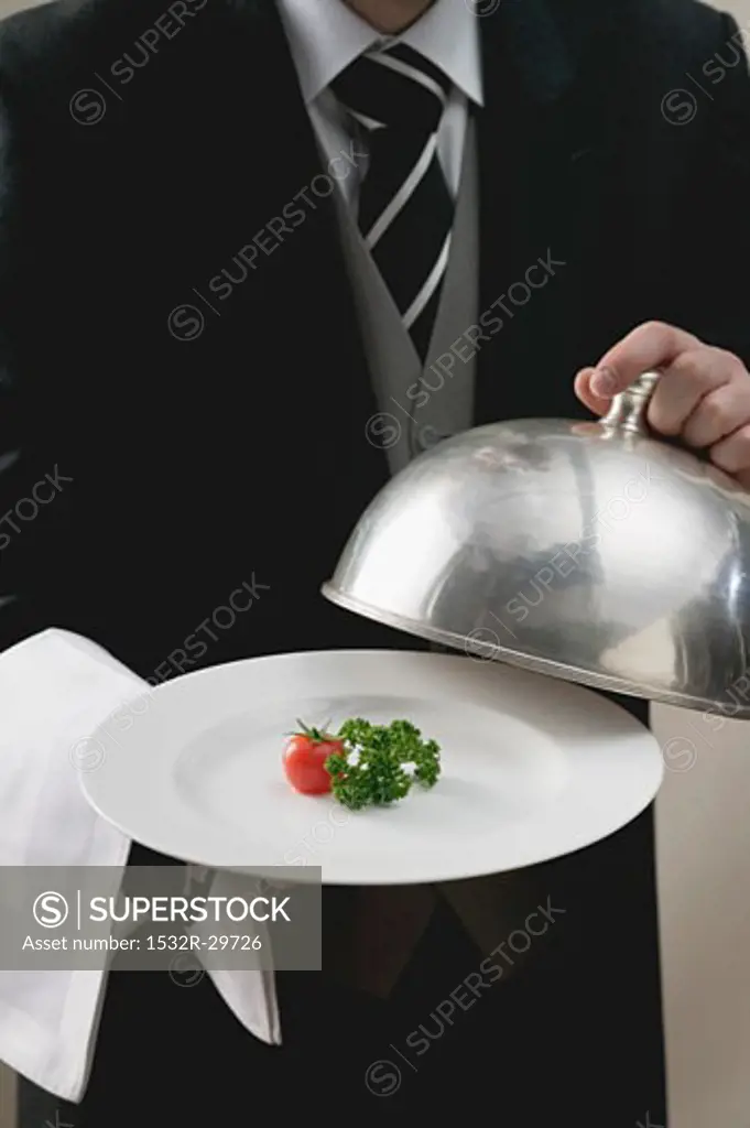 Butler serving tomato and parsley on plate with dome cover