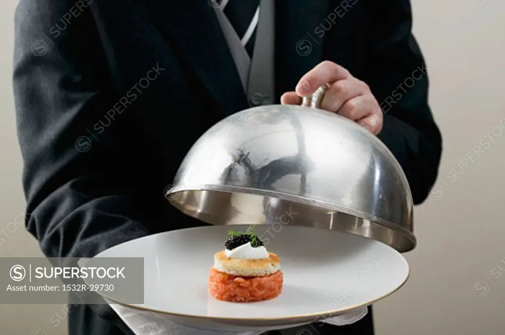 Butler serving salmon tartate on plate with dome cover