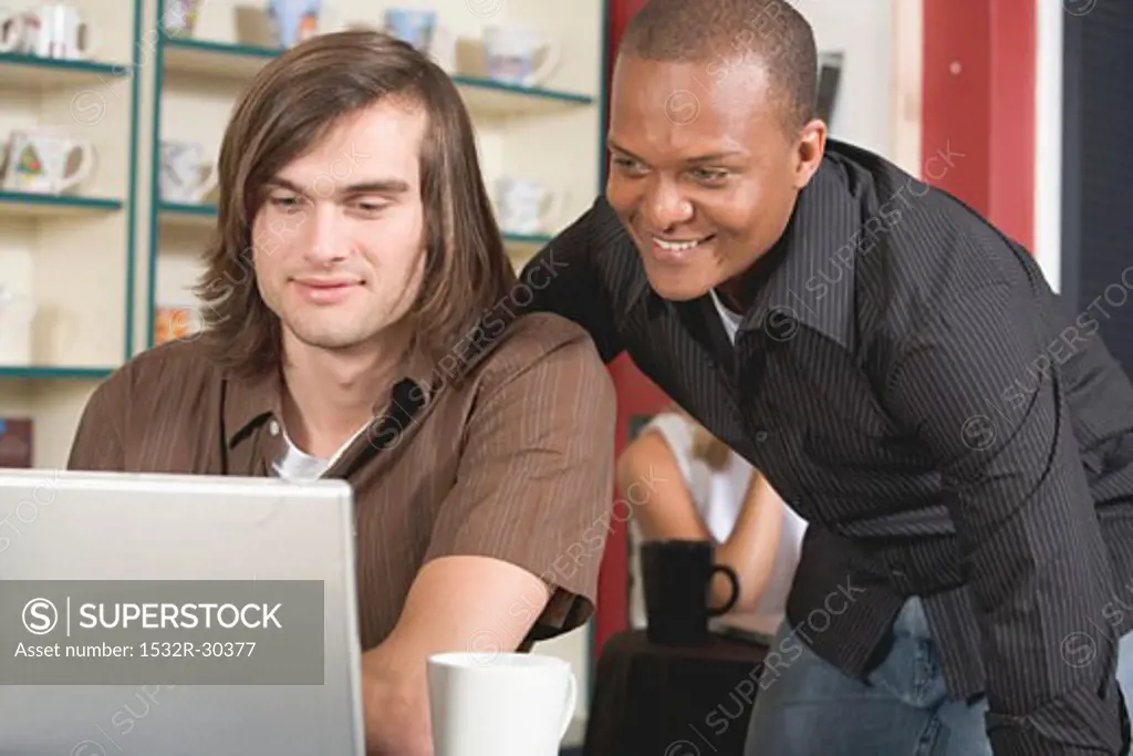 Two men in café looking at a laptop with interest
