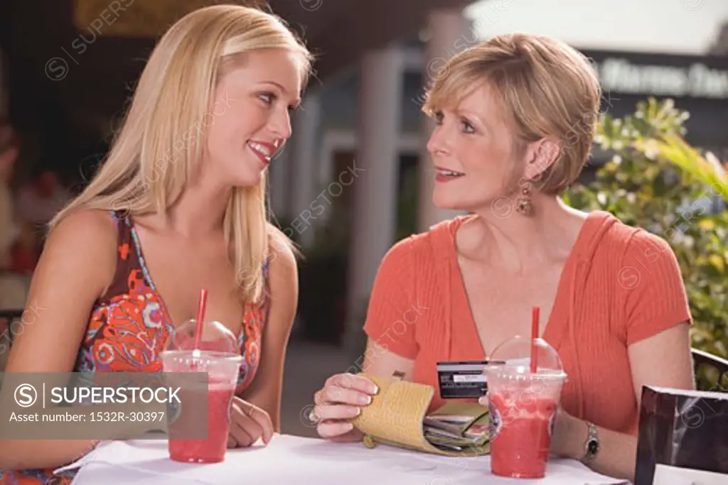 Young woman and mature woman with cold drinks, credit card