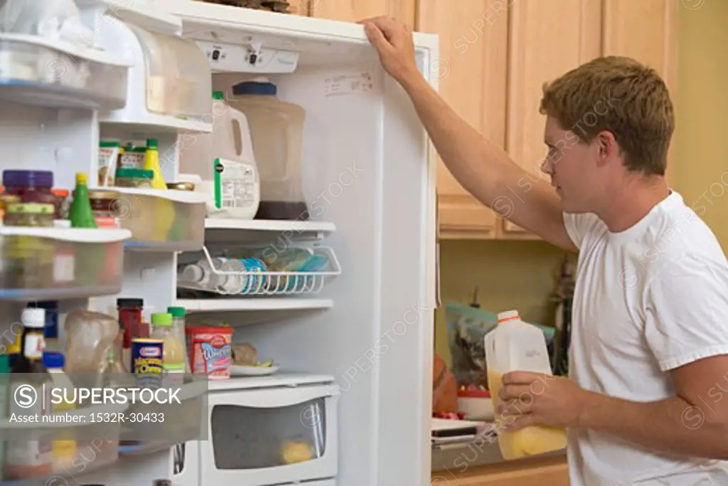 Man in T-shirt examining the contents of his refrigerator